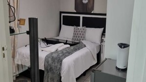 Hotellihuone, jossa on sänky, kattotuuletin, leijonakuva, vedenkeitin ja pieni kaappi.