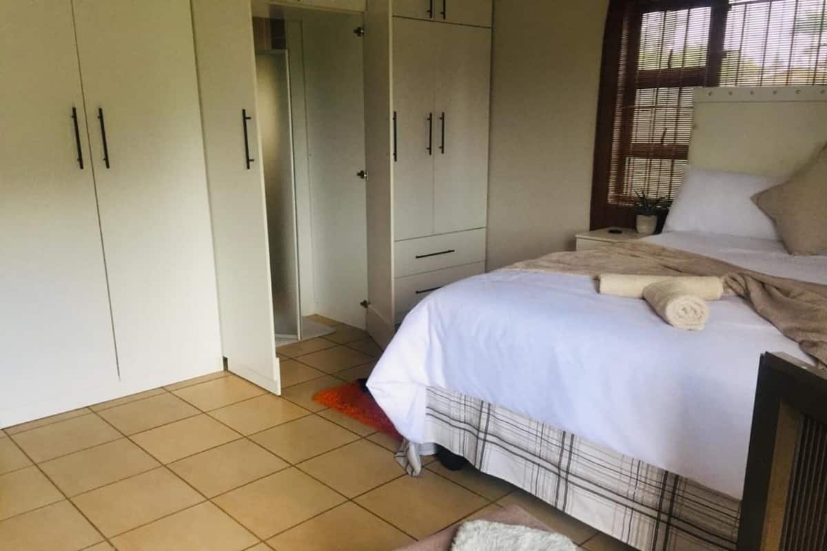 A bedroom with a bed, white curtains, a window, and a wardrobe.