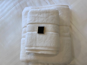 A neatly folded white towel with a black and gold tag, placed on a bed with white bedding.
