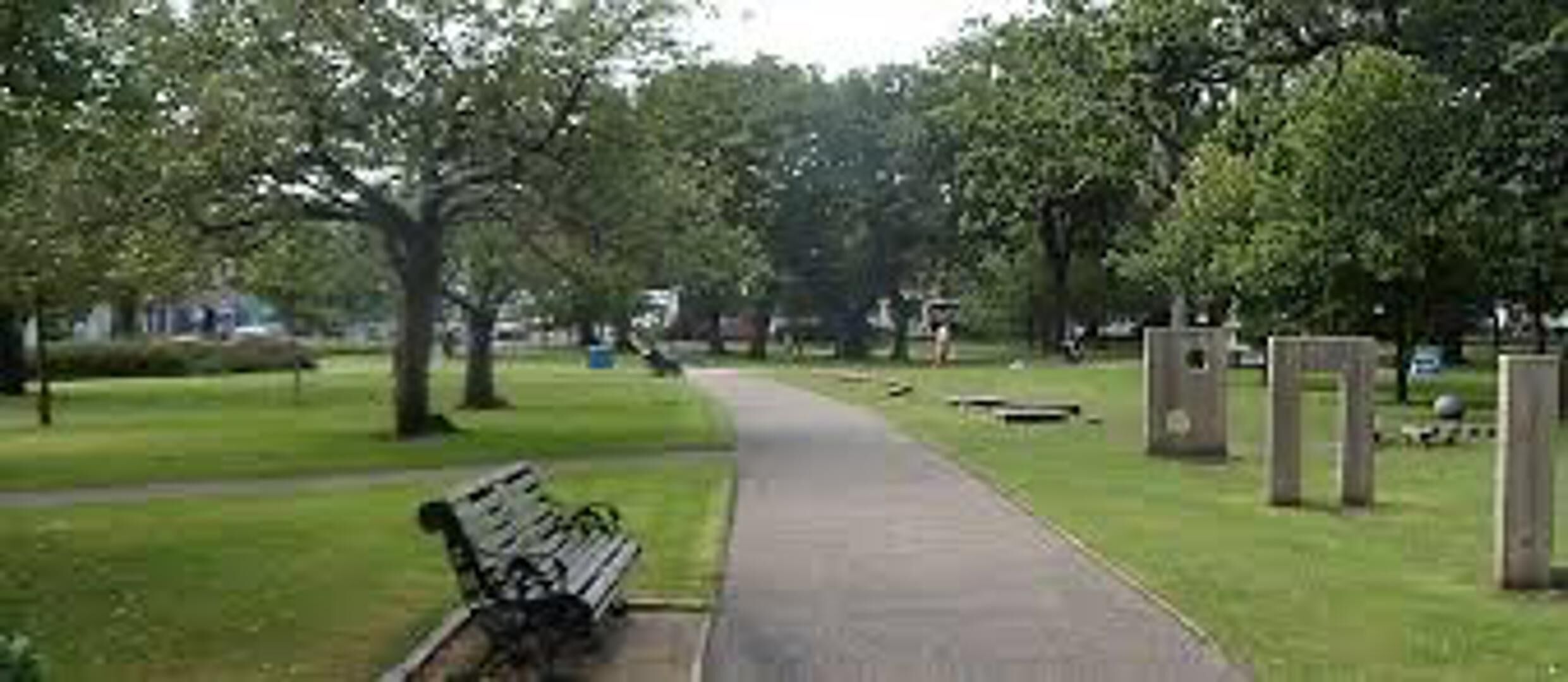 A park with a paved walkway, benches, and trees.