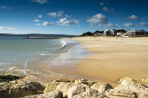 A sandy beach with a rocky foreground and a clear sky.