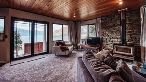 Un salon spacieux avec un mur en pierre, une cheminée, un grand téléviseur et une vue sur un lac.