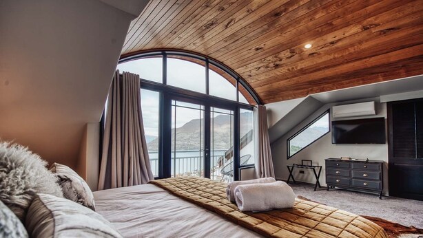 Une chambre avec un grand lit, une vue sur les montagnes, un plafond en bois et un téléviseur fixé au mur.