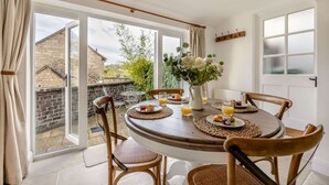 A dining area with a round table, wicker placemats, and chairs. - 2 bedroom Cotswold Holiday Home - Abbots Cottage (Winchcombe)