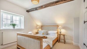 A bedroom with a wooden bed, two bedside lamps, a window with blinds, and a radiator. - 2 bedroom Cotswold Holiday Home - Abbots Cottage (Winchcombe)