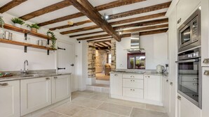 A modern kitchen with white cabinets, a stone countertop, and a wooden ceiling. - 2 bedroom Cotswold Holiday Home - Abbots Cottage (Winchcombe)