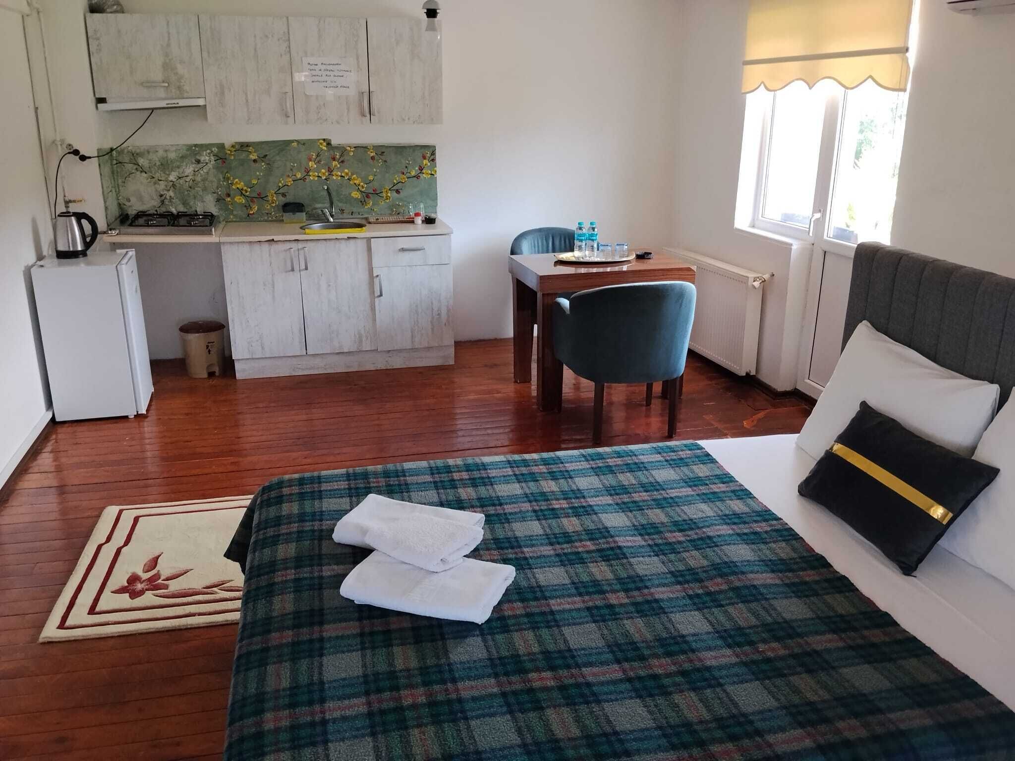 A bedroom with a bed, a desk, a chair, a kitchenette, and a window.