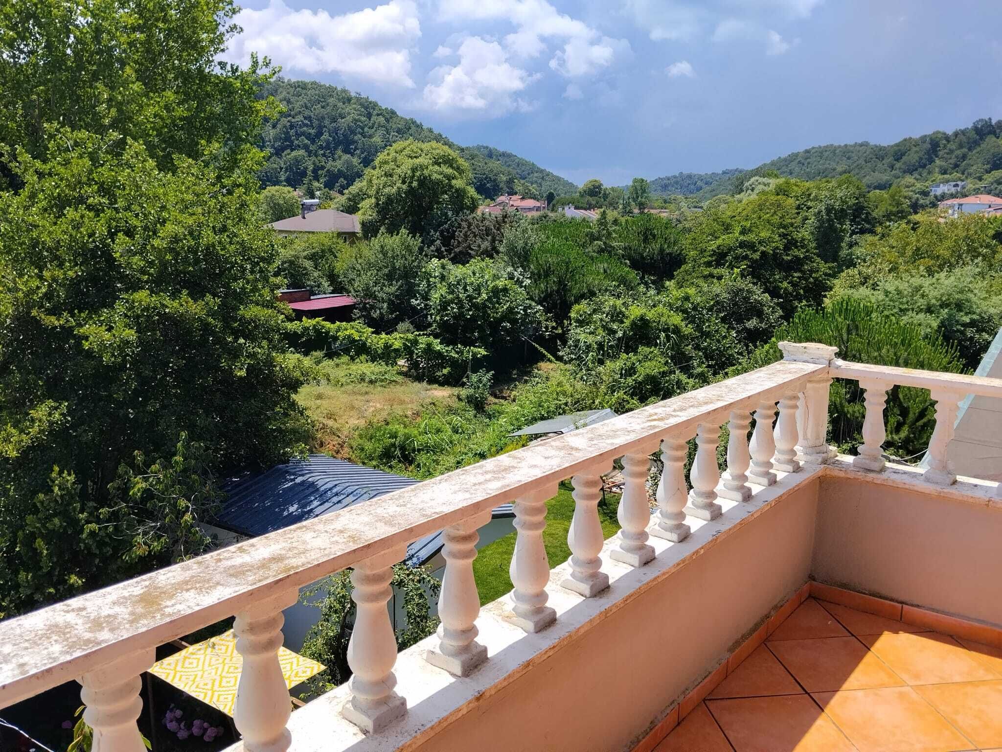 Varanda com balaustrada branca, com vista para uma paisagem verdejante com árvores e casas.