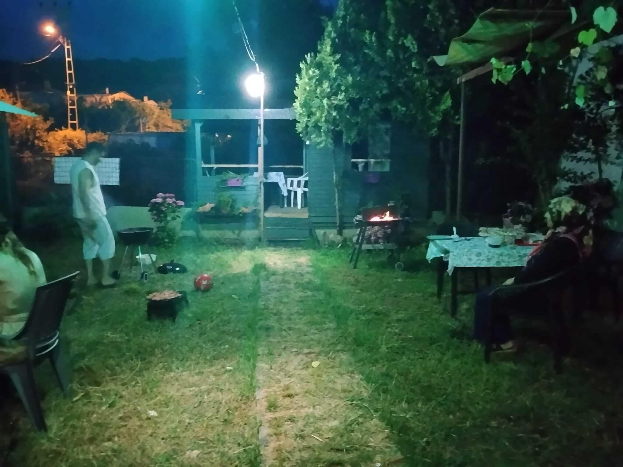 Uma área externa com uma mesa, cadeiras, uma pequena fogueira e uma escada.