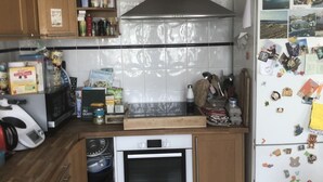 Cocina compacta con armarios de madera, horno integrado, microondas y refrigerador con imanes.