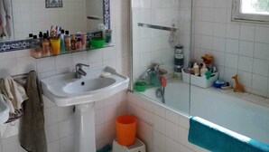 Un baño con lavamanos blanco, espejo y bañera. Hay una ventana sobre la bañera y una cortina de ducha.