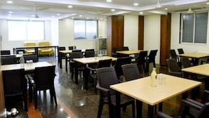Un salón de conferencias con varias mesas y sillas, ventiladores de techo y ventanas amplias.