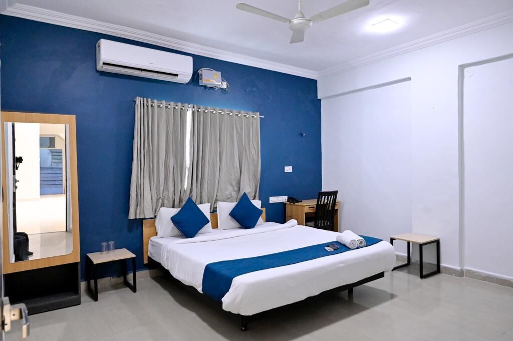 Une chambre d’hôtel équipée d’un lit, d’un bureau, d’une chaise, d’une petite table, d’un miroir et d’un ventilateur de plafond.