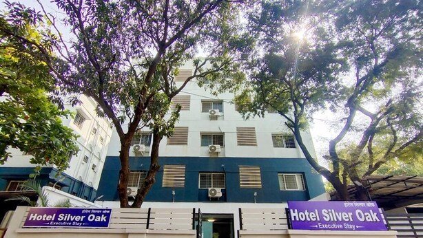 Un edificio con un letrero que indica Hotel Silver Oak, fachada blanca, varias ventanas y un árbol en la parte delantera.