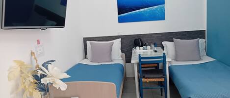 A hotel room with two single beds, a small table with chairs, a TV mounted on the wall, and a decorative plant.