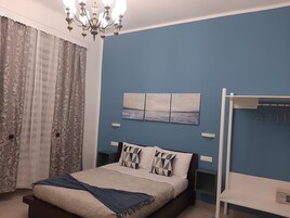 Un dormitorio con cama, una araña, un estante en la pared y un ventanal con cortinas.