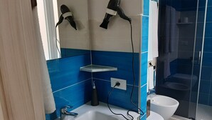 Un baño con lavamanos blanco, espejo, secador de pelo montado en la pared, zona de ducha y inodoro.