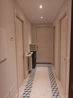 A narrow hallway with a geometric patterned floor, white walls, and doors on both sides.