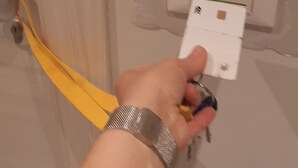 Una mano sosteniendo una llave cerca de la cerradura de una puerta y un interruptor de luz.