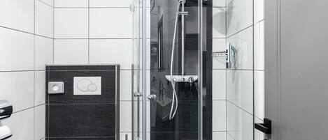 Un baño moderno con ducha envuelta en vidrio, inodoro blanco y tocador con espejo.