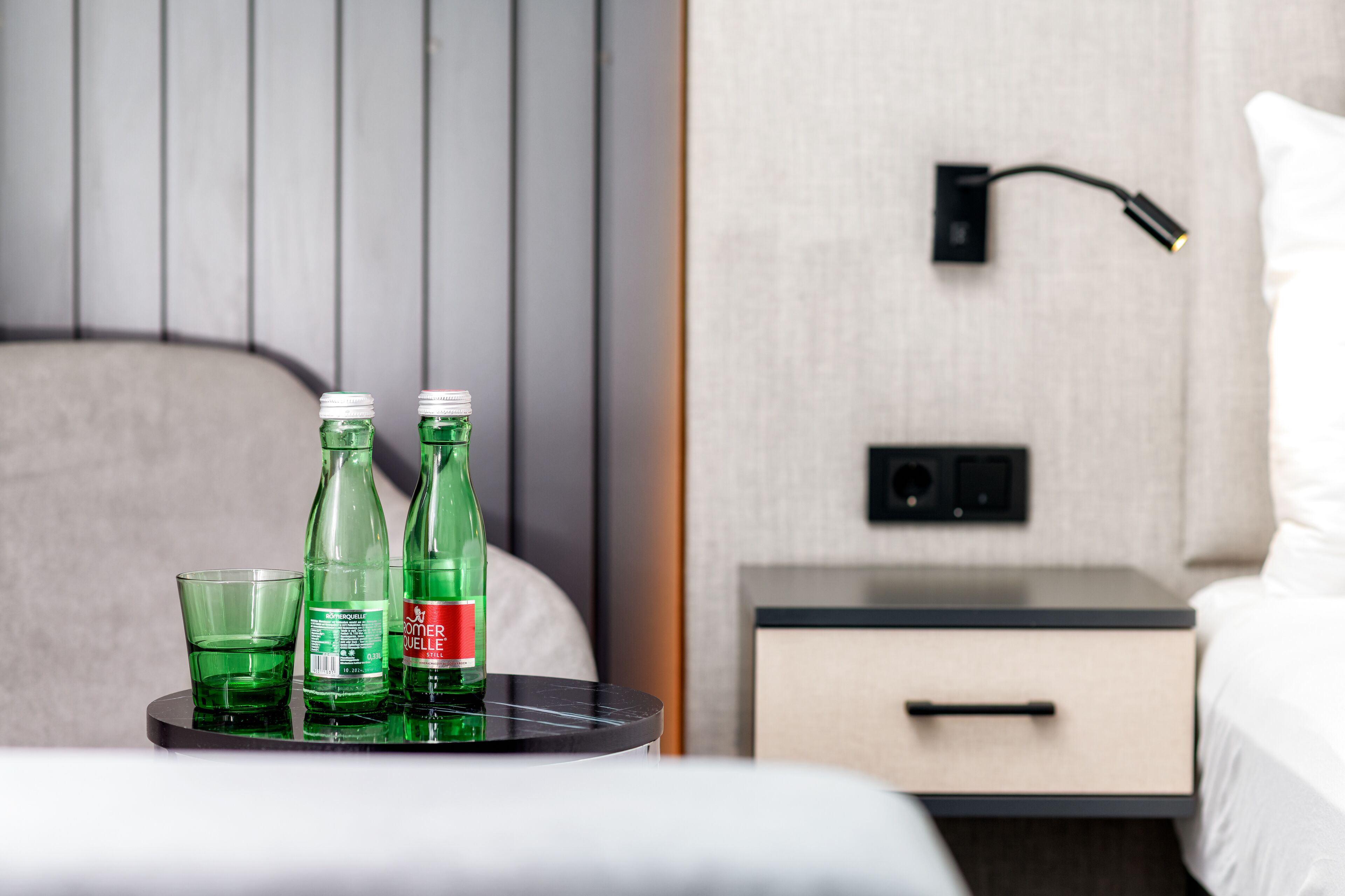Habitación de hotel ordenada con cama, mesita de noche y un velador con lámpara.
