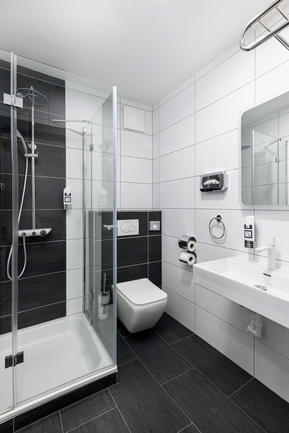 Un baño moderno con ducha envuelta en vidrio, inodoro blanco y lavamanos con espejo.