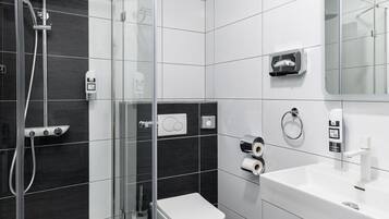 Un baño moderno con ducha envuelta en vidrio, inodoro blanco y lavamanos con espejo.