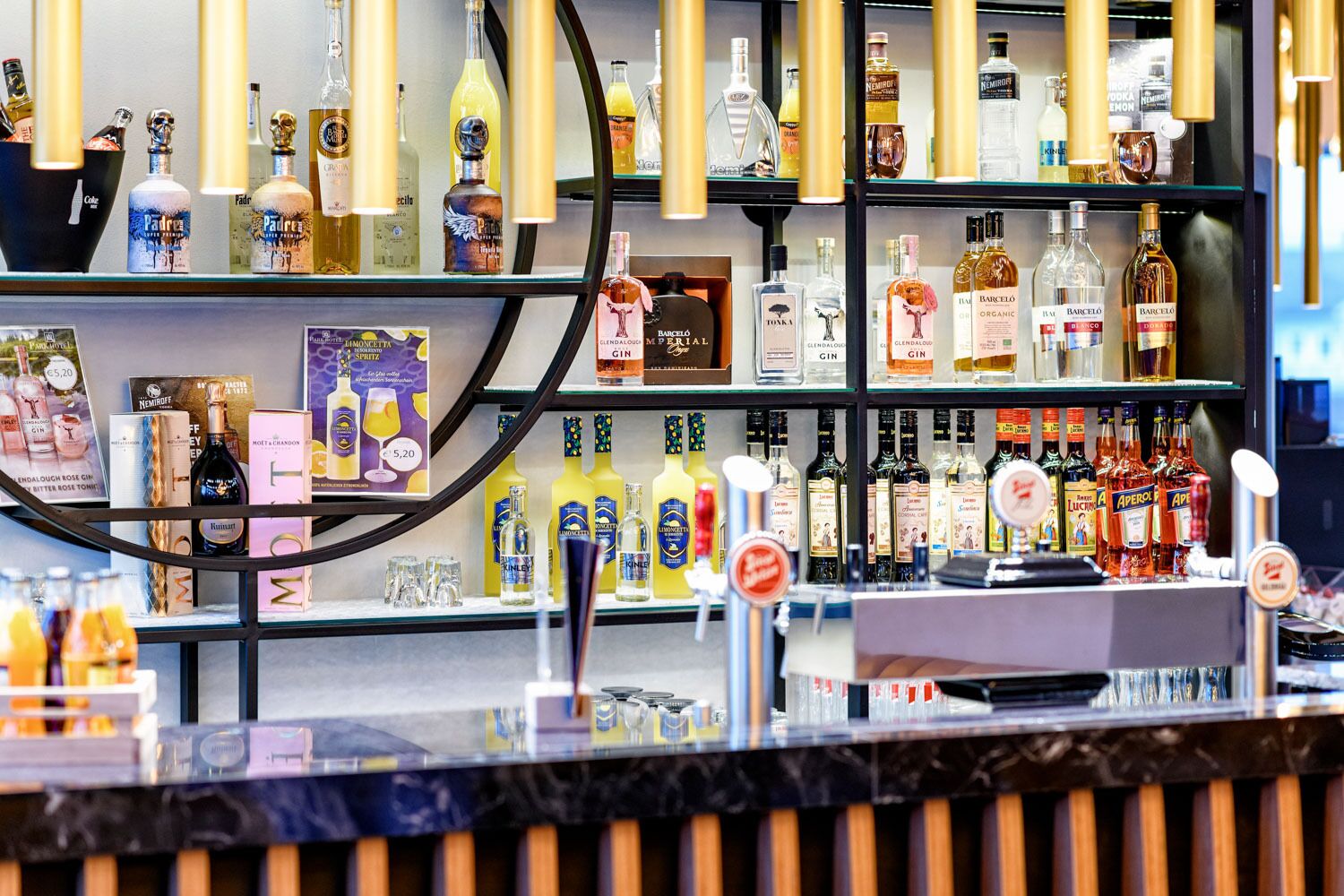 A bar area with shelves of various liquor bottles and a counter with glasses and a tap.