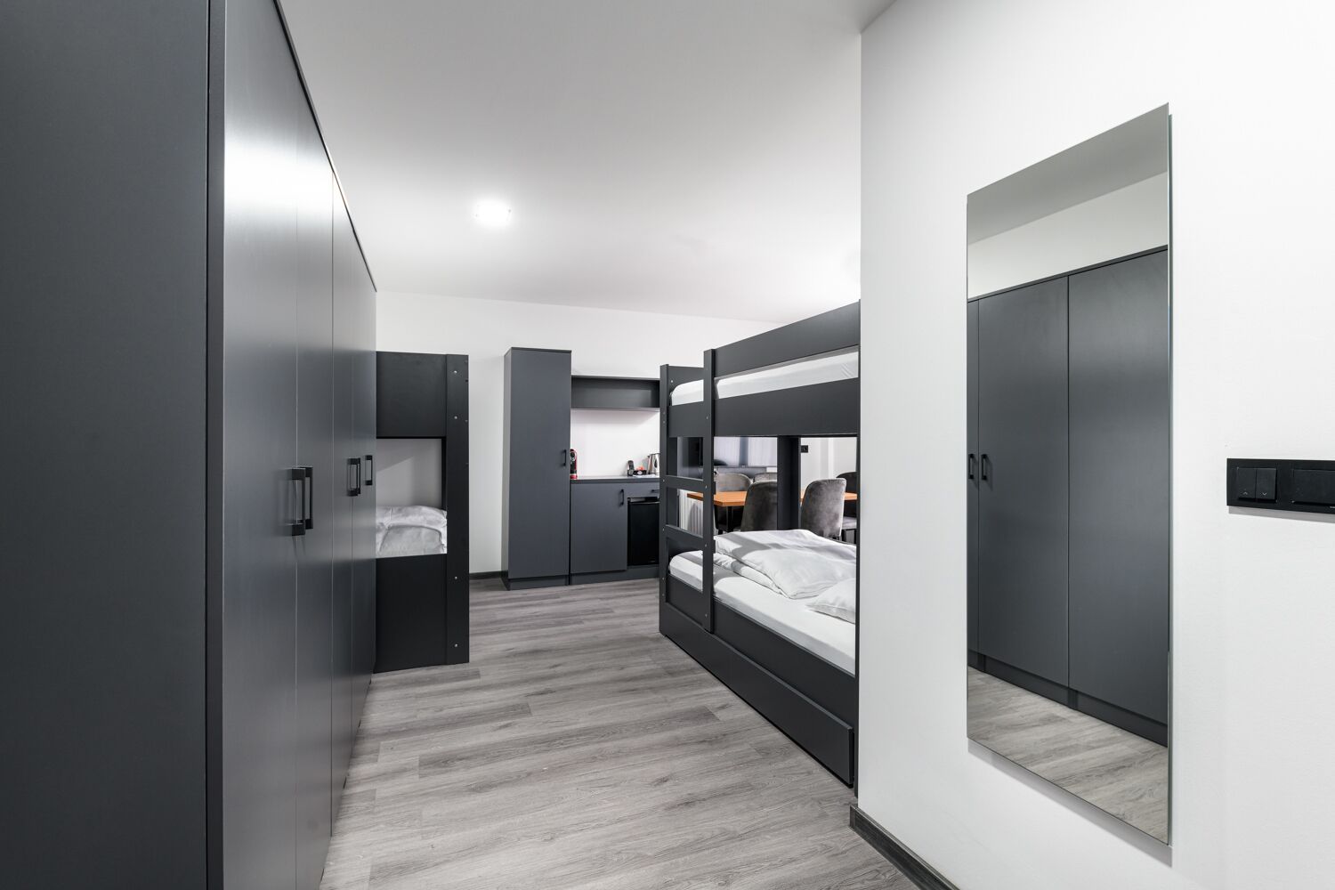 Una habitación de hotel moderna con literas, kitchenette y un espejo grande.
