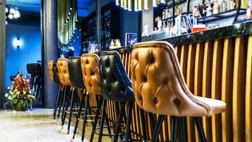 Eine Reihe von Barhocker mit gestopften Ledersitzen und schwarzen Metallbeinen, vor einer Bar mit einer Holzpaneelenwand und einer blauen Wand im Hintergrund.