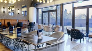 A modern hotel lobby with round tables, leather seating, and a large window offering a view of the outside. - Parkhotel Braunau  (Braunau am Inn)