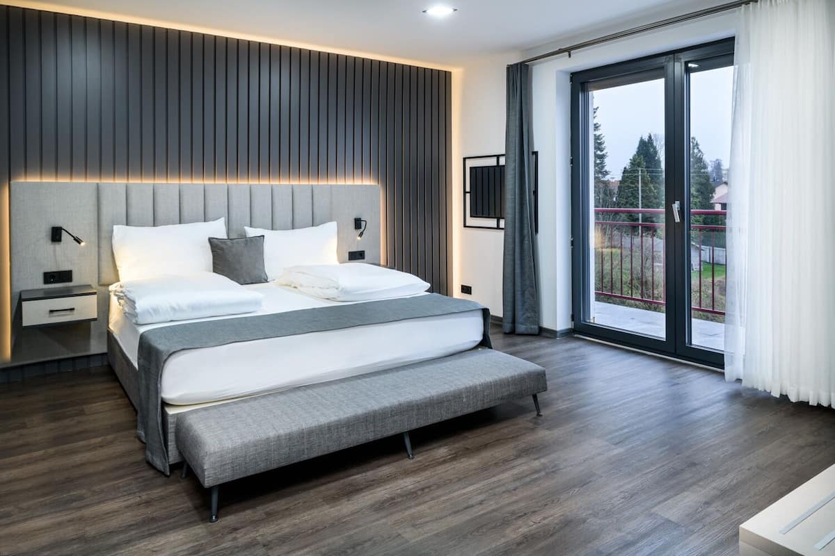 A modern bedroom with a large bed, a nightstand, a TV mounted on the wall, and a sliding glass door to the outside.