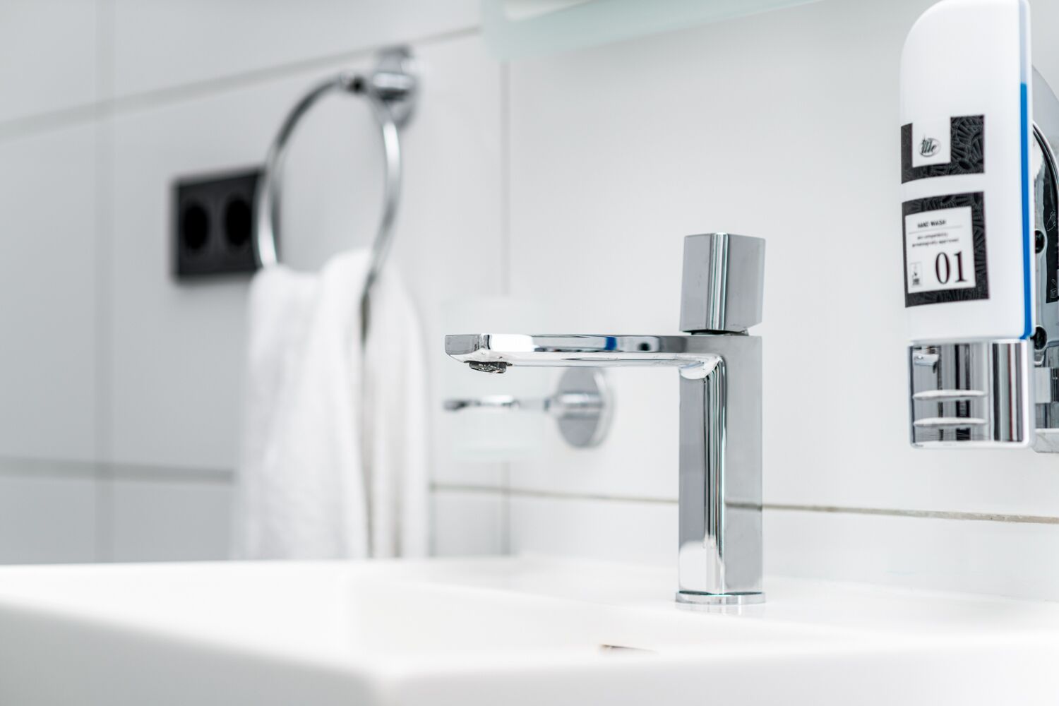 Un baño moderno con grifo de cromo, un perchero y un dispensador de jabón.