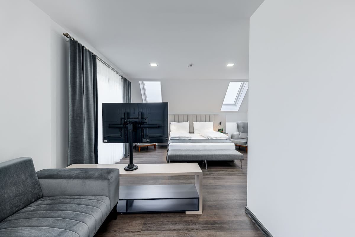 A modern hotel room with a sofa, a TV, a bed, and a desk.