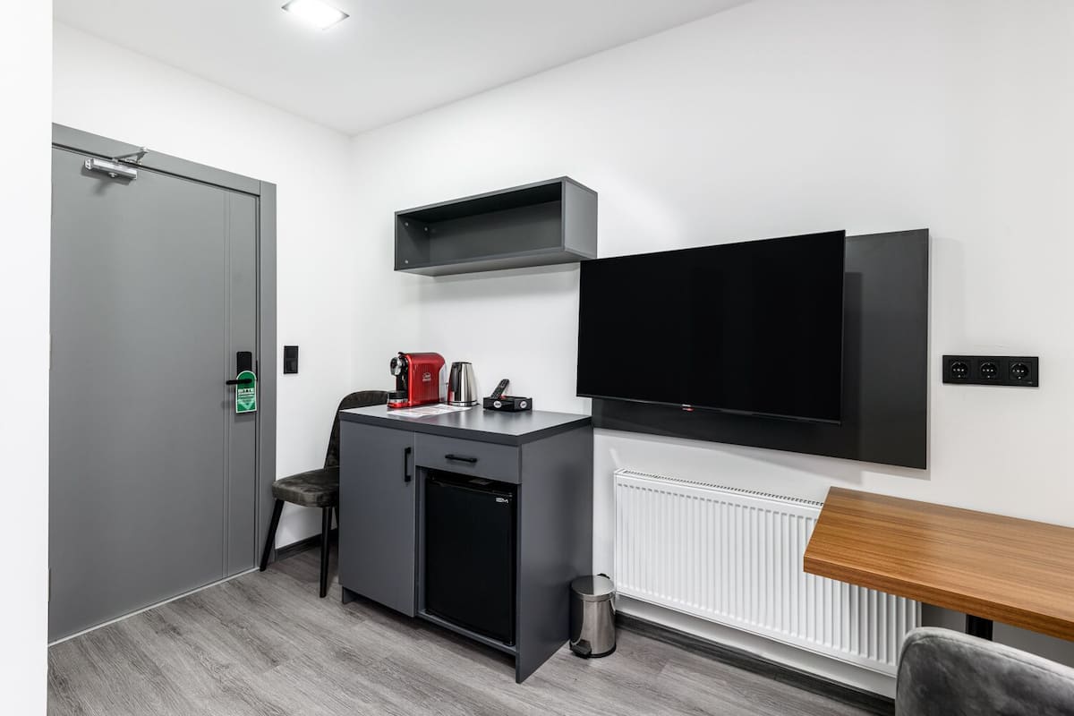 A compact room with a kitchenette, a flat-screen TV mounted on the wall, a small cabinet, and a radiator.