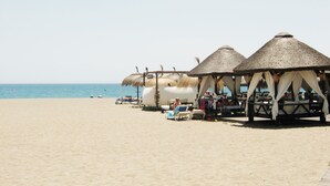 Uma praia com palafitas de telhado de palha e espreguiçadeiras.