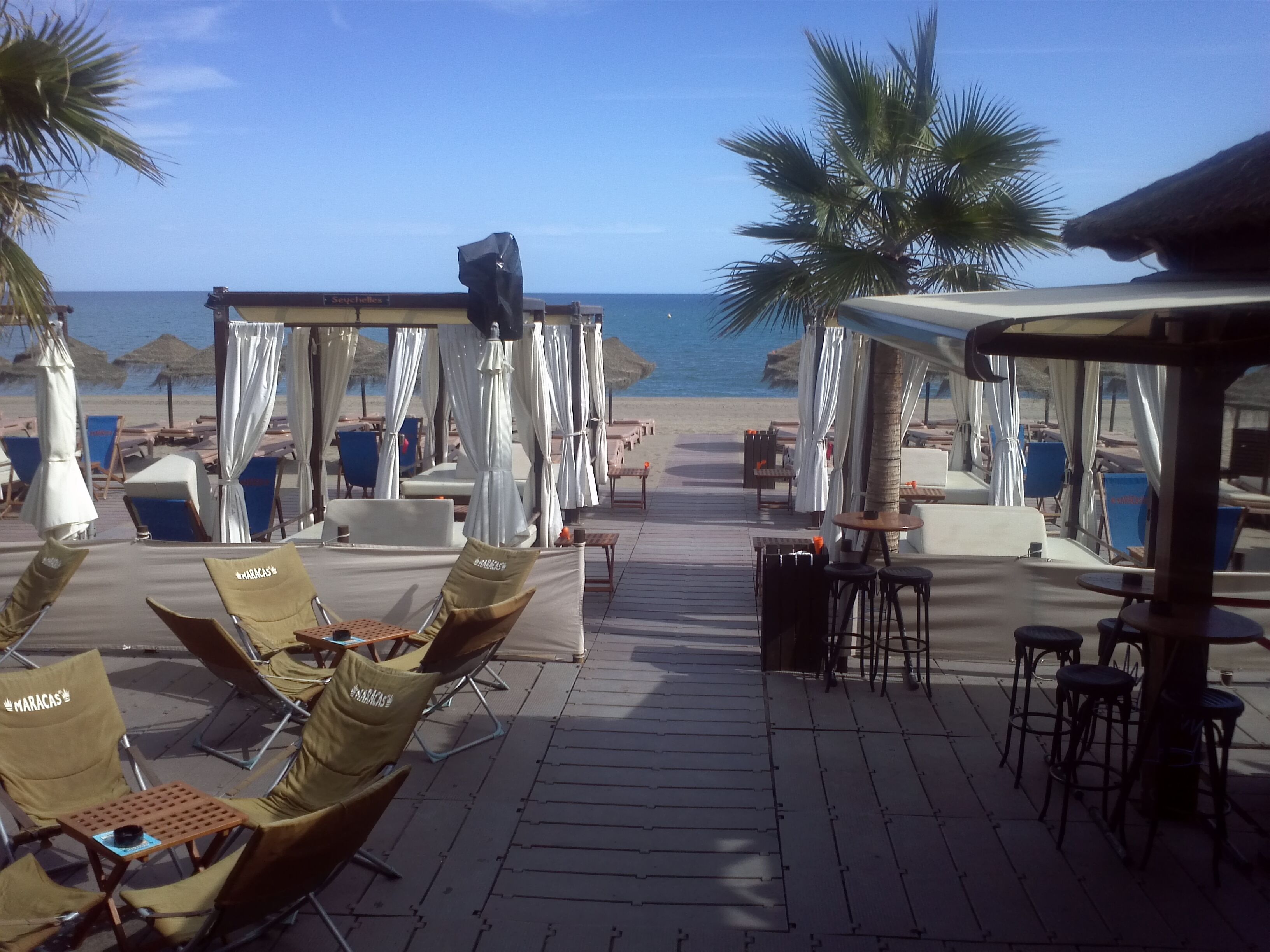 A beachside patio with lounge chairs and umbrellas, a wooden deck, and a view of the ocean.