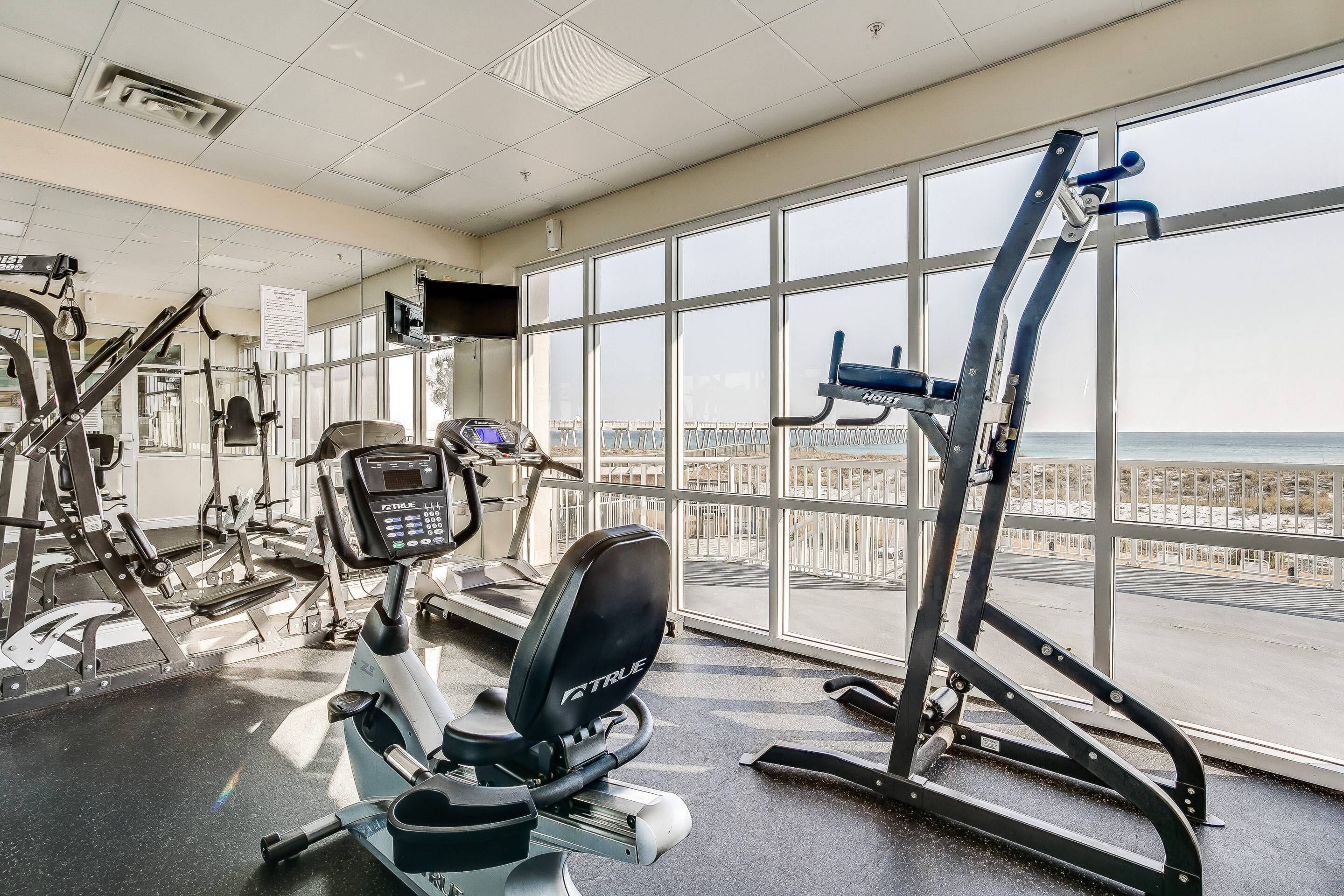 A gym with various exercise equipment, large windows, and a view of the beach.
