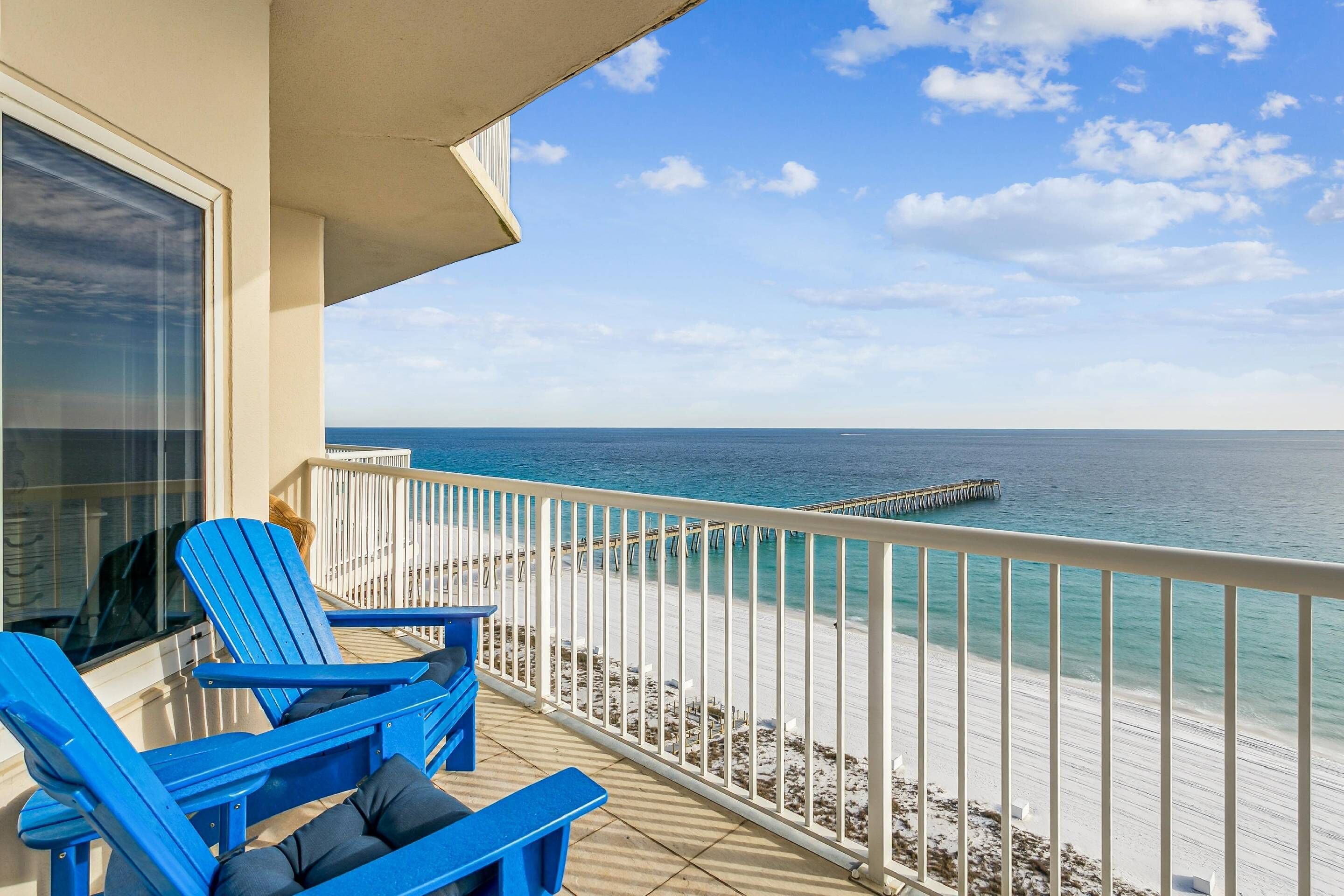 A balcony with blue chairs and a view of the ocean.