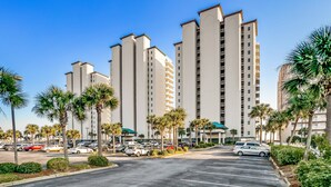 A multi-story parking lot with several cars parked, surrounded by palm trees and a large building with multiple balconies. - Stay 5 Nights this Summer at Summerwinds West |15th Floor W/ Breathtaking Views |Beach Set Included (Navarre)