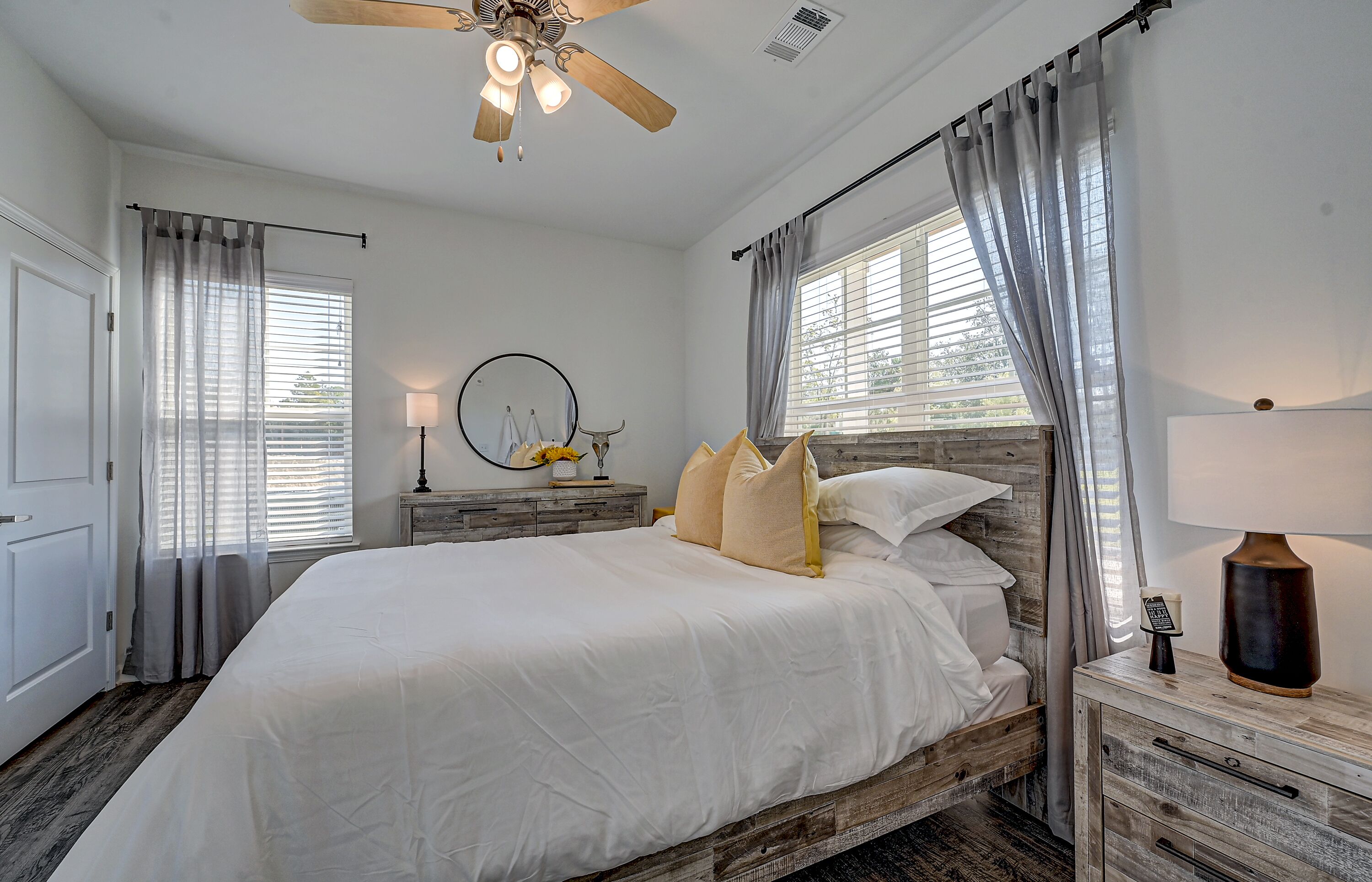 A bedroom with a wooden headboard, a bed with white bedding, a nightstand with a lamp, and a ceiling fan.