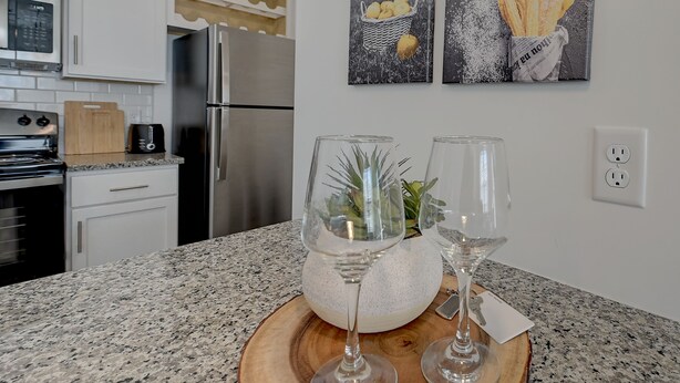 A kitchen with a granite countertop, a wooden cutting board, two wine glasses, and a decorative vase with a plant. - PrimRose Retreat in Orange Pk Nr. NAS JAX& ENTMT. (Jacksonville)