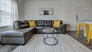 A modern living room with a sectional sofa, a round coffee table, and a yellow stool. - PrimRose Retreat in Orange Pk Nr. NAS JAX& ENTMT. (Jacksonville)