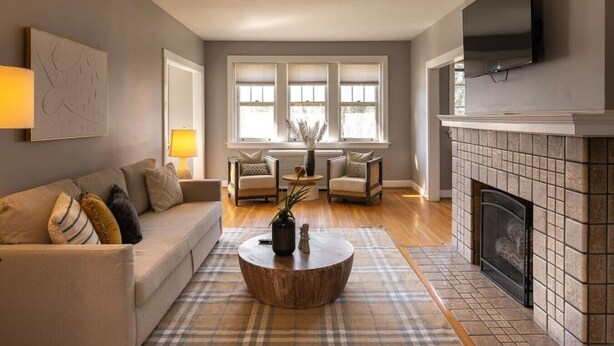 A living room with a sofa, armchairs, a coffee table, a fireplace, and a TV mounted on the wall. - Spacious in Hyde Park with Patio (Cincinnati)