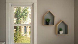 A window with a view of greenery and buildings, two wall-mounted plant holders with plants, and a white window frame. - Spacious in Hyde Park with Patio (Cincinnati)