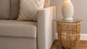 A beige sofa with a textured throw pillow, a woven side table with a lamp, and a plaid rug on a wooden floor. - Spacious in Hyde Park with Patio (Cincinnati)