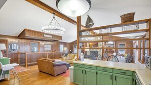 A spacious living area with wooden floors, a green kitchen, and a high ceiling with a chandelier. - Spacious 6BR Greene Lodge on Lake Keowee, perfect for family getaways! (Six Mile)