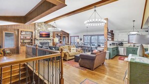 A spacious living area with a wooden staircase, a stone fireplace, and a dining area with a chandelier. - Spacious 6BR Greene Lodge on Lake Keowee, perfect for family getaways! (Six Mile)