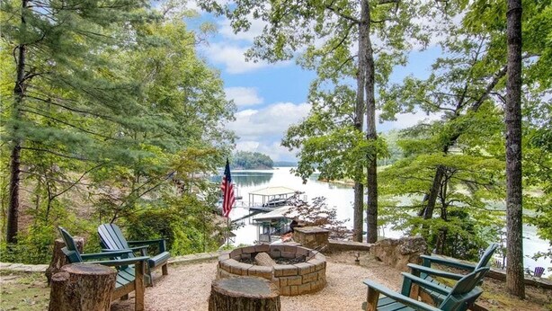 A lakeside seating area with Adirondack chairs, a fire pit, and a dock with a covered structure. - Spacious 6BR Greene Lodge on Lake Keowee, perfect for family getaways! (Six Mile)