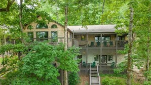 A two-story cabin with a balcony, surrounded by dense forest. - Spacious 6BR Greene Lodge on Lake Keowee, perfect for family getaways! (Six Mile)